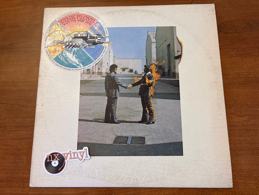 Vinyl record cover with two people shaking hands on a street, featuring a 'Pink Floyd' logo.
