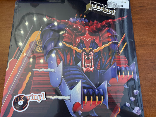 Vinyl record cover with a dragon design and 'Judas Priest' branding on a wooden surface.