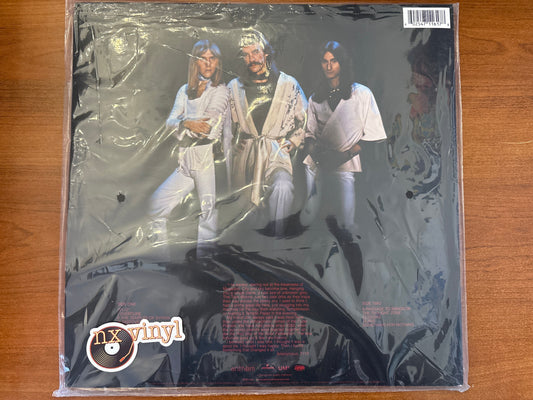 Vinyl record in packaging with a cover featuring three people, on a wooden surface.
